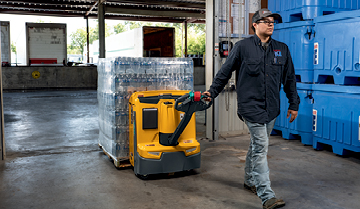 Worker pulling Jungheinrich walkie pallet truck loaded with bottles through warehouse